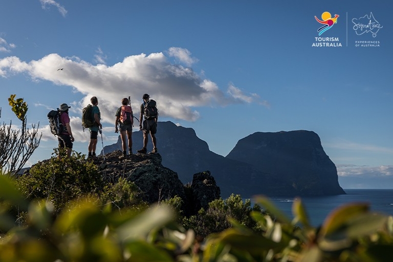 A small group of hikers stand atop of hill looking towards Mt Gower on Lord Howe Island, New South Wales © Pinetrees Lodge / Seven Peaks Walk 