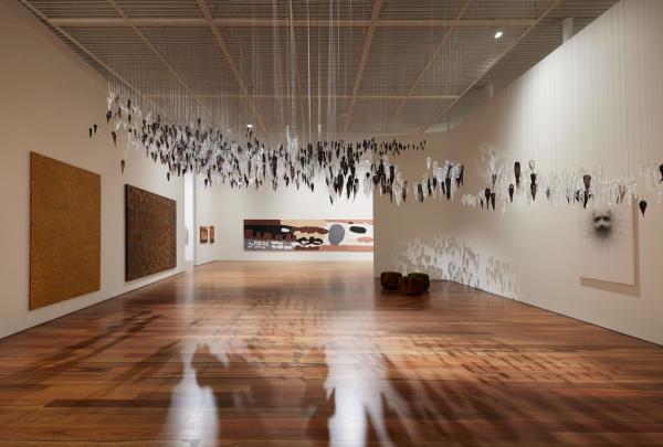 At the Art Gallery of New South Wales, Sydney, a spacious gallery displays Aboriginal and Torres Strait Islander art. Dozens of dark, pointed sculptures hang from the ceiling above polished timber floors and large wall paintings. © Tourism Australia