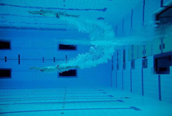 An underwater view of a swimmer at the Australian Institute of Sport's aquatic centre. The swimmer is captured in mid-stroke, trailing a long, artistic wake of bubbles through the deep blue water of a professional Olympic-sized lane.  © Tourism Australia