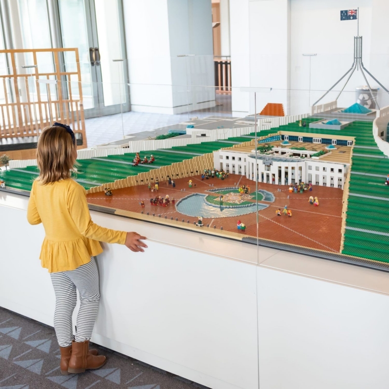 In the heart of Canberra's Capital Hill, a child gazes in wonder at a massive Lego sculpture of the Australian Parliament House. The intricate replica stands proudly inside the actual Parliament House, capturing the essence of this iconic Australian landmark in vibrant, interlocking bricks. The child's awe-filled expression reflects the magic of this miniature masterpiece within the nation's political centre © Tourism Australia