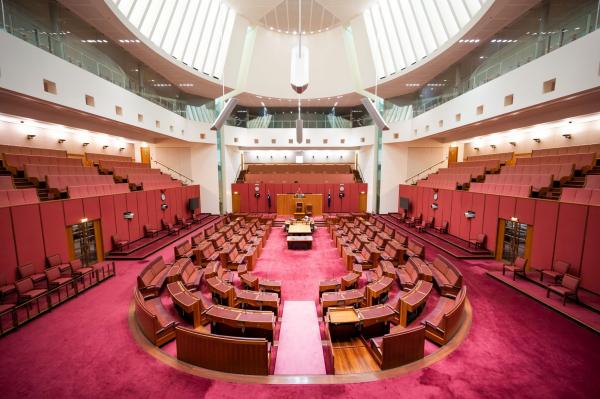 interior of the Senate Chamber in the Australian Parliament House located in Canberra, specifically on Capital Hill. The room exudes an aura of authority and democracy, with its polished wooden desks, leather seats, and a central table for parliamentary proceedings. The chamber is bathed in soft, natural light, emphasising its grandeur and historical significance in Australian politics. © Tourism Australia