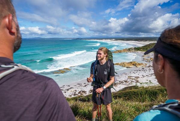 A group of avid walkers on the Bay of Fires Signature Walk, taking in the stunning view. With packs on their backs, they walk along the pristine coastline, Bay of Fires, Tasmania © Great walks of Australia