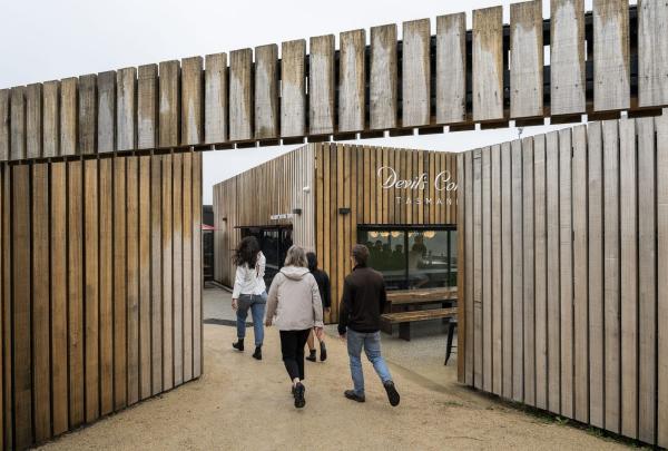 At the Devil’s Corner cellar door on the East Coast of Tasmania, visitors walk through a striking, modern entrance made of vertical timber slats that lead into a stylish courtyard with contemporary wood-clad buildings. © Tourism Australia