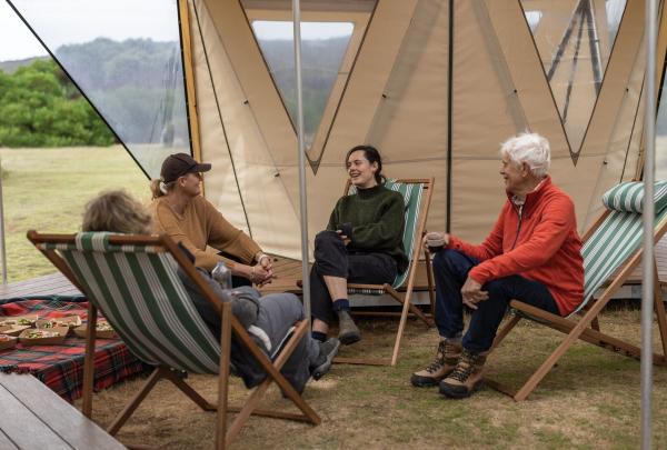 Guests relax in striped deck chairs at the exclusive Eco-Comfort Camp on a Flinders Island Walking Adventure in Comfort, Tasmania. The communal tent features a unique triangular design and panoramic views of the rugged outback. © Tourism Australia