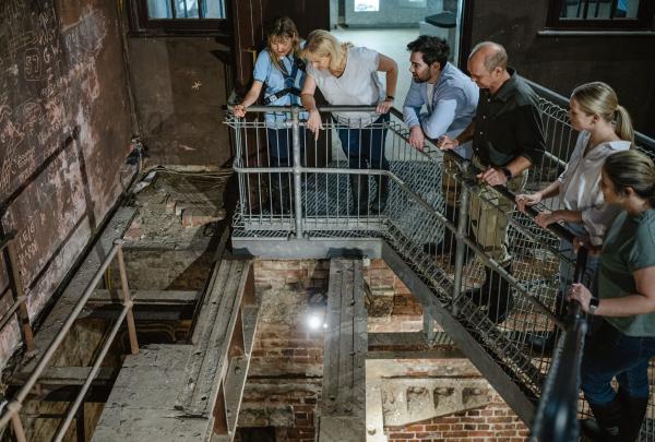 A group of visitors on a Fremantle Prison Tunnels tour in Perth, Western Australia, peers over a metal railing into a dark, historic shaft. Guided by an expert, they explore the weathered brickwork of this heritage site. © Tourism Australia