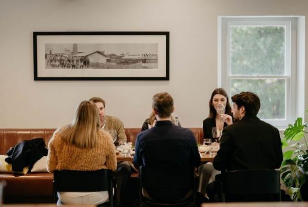 Guests sit around a wooden table in the bright, modern tasting room at Hardys Tintara in McLaren Vale, South Australia. Large windows and lush indoor plants create a relaxed atmosphere for enjoying a premium wine-tasting experience. © Hardys Tintara