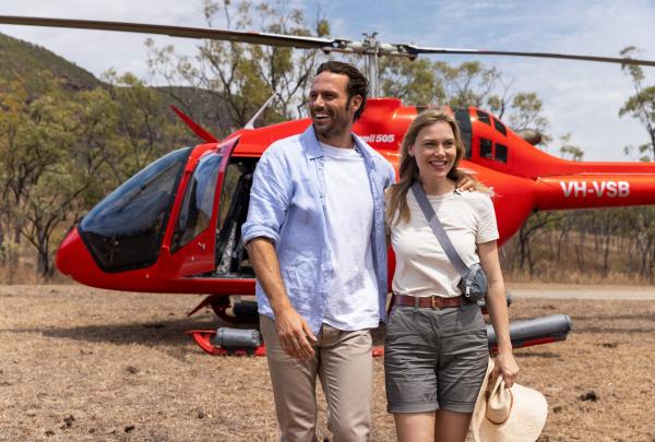 Guests step out from a vibrant red helicopter after landing with Jarramali Rock Art Tours. Smiles light up their faces as they happily take in the breathtaking scenery of Outback Queensland, Cook, Queensland © Tourism Australia