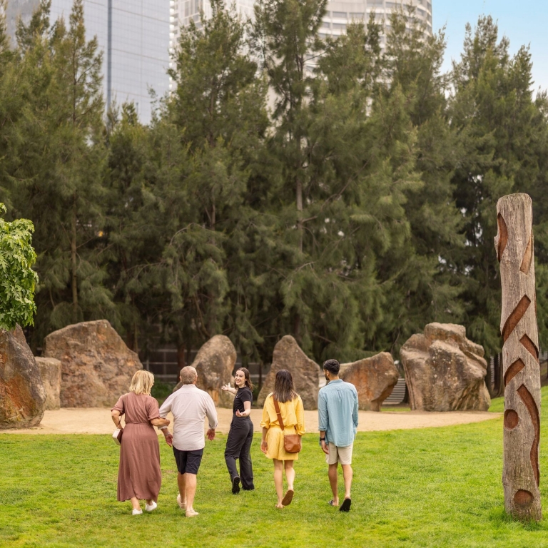 The image captures a group of engaged participants on the Birrarung Wilam Walk Tour, commencing at Federation Square. Against the urban backdrop, the tour progresses to the Birrarung Wilam (River Camp) Aboriginal art installations, Birrarung Wilam to the Kulin Nation, Koorie Heritage Trust, Melbourne, Victoria © Tourism Australia