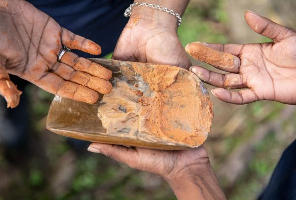 Hands showing ochre paint on wooden artefact for women's welcome to country ceremony, Mandingalbay Authentic Indigenous Tours, Cairns, Queensland © Tourism Australia