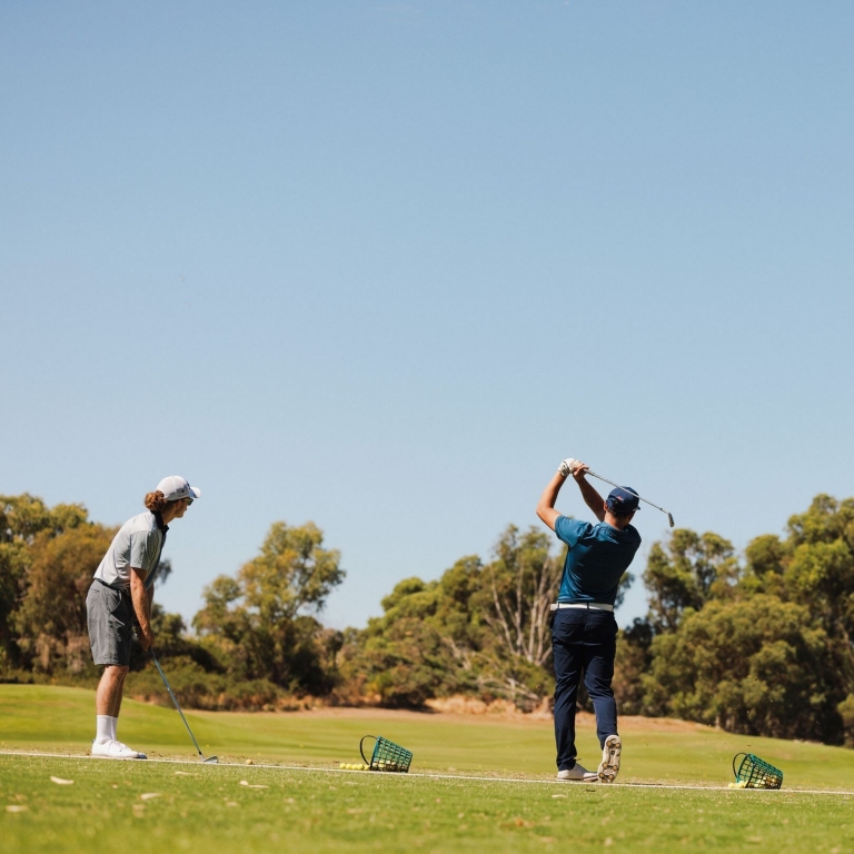 Golfers sharpen their skills at the practice range of Meadow Springs Golf and Country Club in Meadow Springs, Western Australia. The expansive facility allows players to warm up against a backdrop of the region's signature Tuart trees and clear blue skies, reflecting the club's commitment to a premium golfing experience. © Tourism Australia