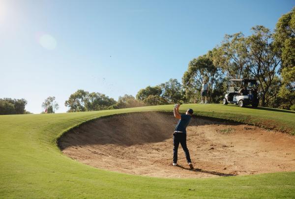 A golfer executes a crisp bunker shot at Meadow Springs Golf and Country Club in Meadow Springs, Western Australia. The course is renowned for its "golf as nature intended" philosophy, featuring large, strategically placed bunkers and fairways lined with majestic, 200-year-old Tuart trees. © Tourism Australia