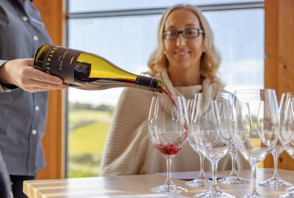 Woman sitting at a table, watching a tasting glass be pured of red wine at Montalto, Red Hill South, Mornington Peninsula, Victoria © Tourism Australia