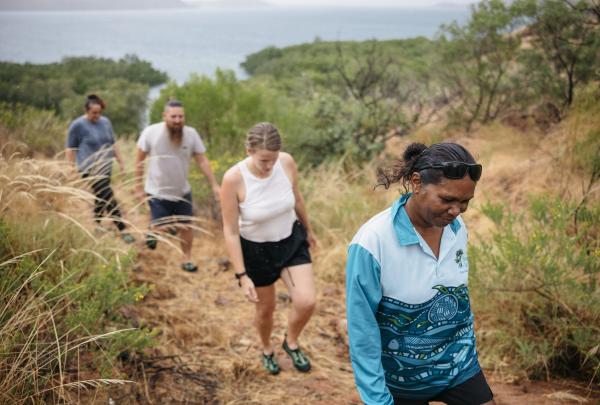 An indigenous guide walks with three tour attendees against a coastal backdrop on Oolin Sunday cultural tours, Northern Territory © Tourism Australia