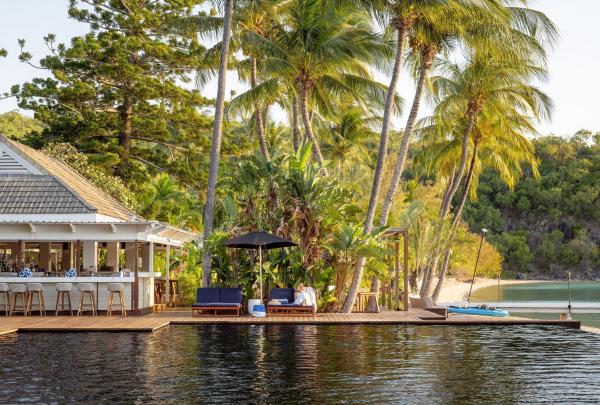 In the late afternoon sunshine, a person relaxes by the pool at Orpheus Island Resort. The pool glistens in the warm light, inviting and calm. To the side, the pool bar adds a laid-back tropical vibe. Behind them, the palm-lined beach stretches out toward the ocean, completing the idyllic island setting. © Tourism Australia
