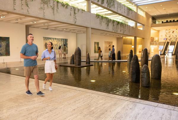 Visitors stroll through the light-filled, spacious galleries of the Queensland Art Gallery of Modern Art (QAGOMA). People move thoughtfully from one exhibit to another, pausing to admire the diverse range of sculptures and paintings. Their faces reveal expressions of wonder and awe, reflecting the captivating and inspiring artworks that surround them in this modern cultural space. © Tourism Australia
