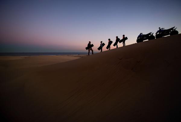 Guests on the Sand Dune Adventures tour at Stockton Beach silhouetted against a pink sunset with two quad bikes, Sand Dune Adventures, Stockton Beach, Port Stephens, New South Wales © Tourism Australia