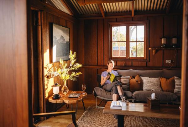 A hiker relaxes on a comfortable lounge inside their accommodation after a long day on the Scenic Rim Trail. Soft natural light filters through the window, creating a calm and peaceful atmosphere. The hiker is stretched out with a book in hand, fully absorbed in reading. The quiet space offers a perfect moment of solitude, allowing them to unwind, recharge, and enjoy a well-earned rest surrounded by the stillness of nature. © Tourism Australia