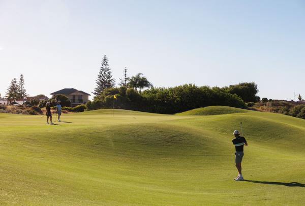 A group of golfers plays a round on the sun-drenched fairways of Secret Harbour Golf Links in Secret Harbour, Western Australia. This traditional Scottish-style course features rolling terrain and strategic bunkering, set within a coastal landscape south of Perth. © Tourism Australia