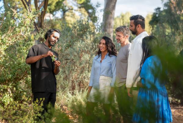 An Indigenous tour guide from Southern Cultural Immersion leads a group through Adelaide Botanic Gardens and gestures towards various plant species, Adelaide, South Australia © Tourism Australia