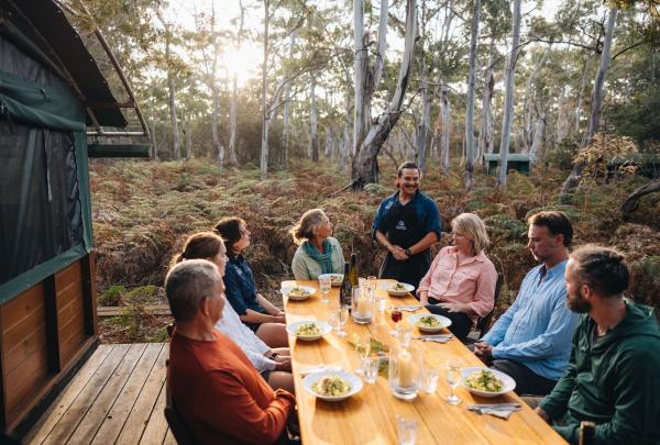 A group of people enjoy a relaxing meal together beside their accommodation huts during their adventure with The Maria Island Walk on Maria Island, Tasmania © Tourism Australia