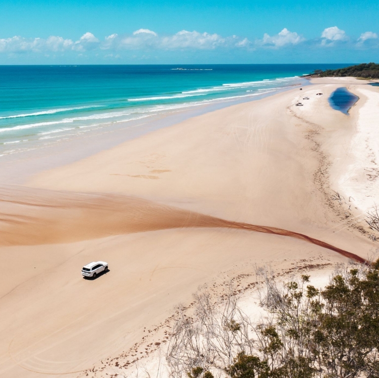 Yura tours 4WD cruising down beach with teatree creek flowing out to ocean, Minjerribah/North Stradbroke Island, Queensland © Tourism Australia